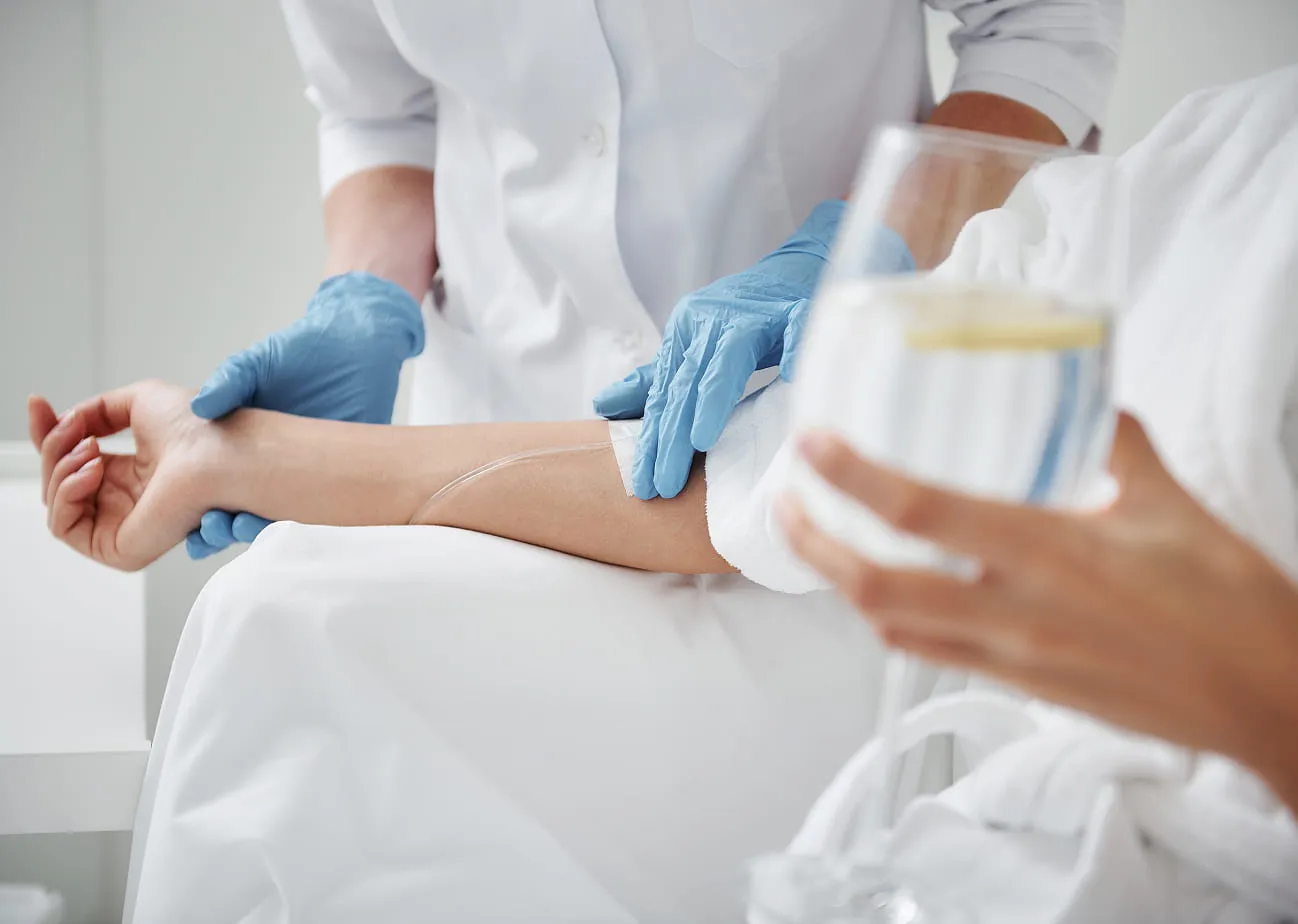 Patient in a white robe receiving a wellness infusion from a clinician wearing blue gloves