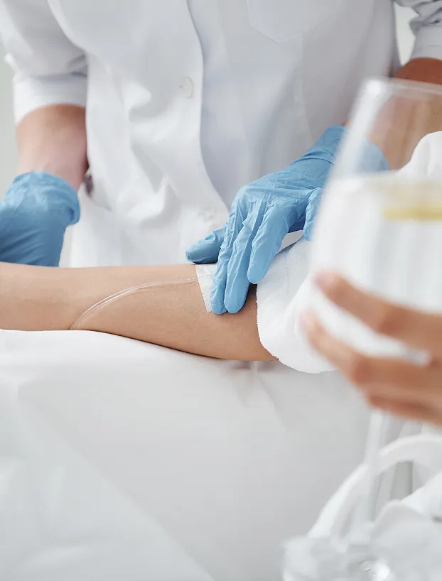 Healthcare professional in blue gloves preparing a patient's IV infusion in a clinical setting