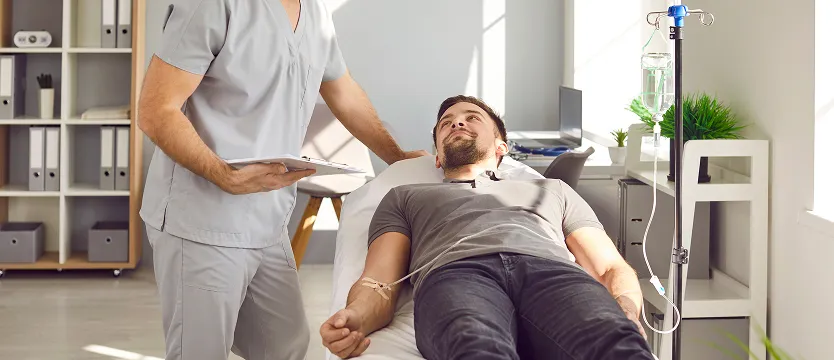 Patient receiving infusion therapy while a healthcare professional reviews their chart in a comfortable clinical setting