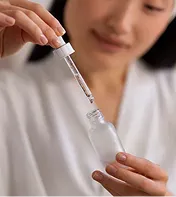 Woman using skincare serum dropper in a wellness setting